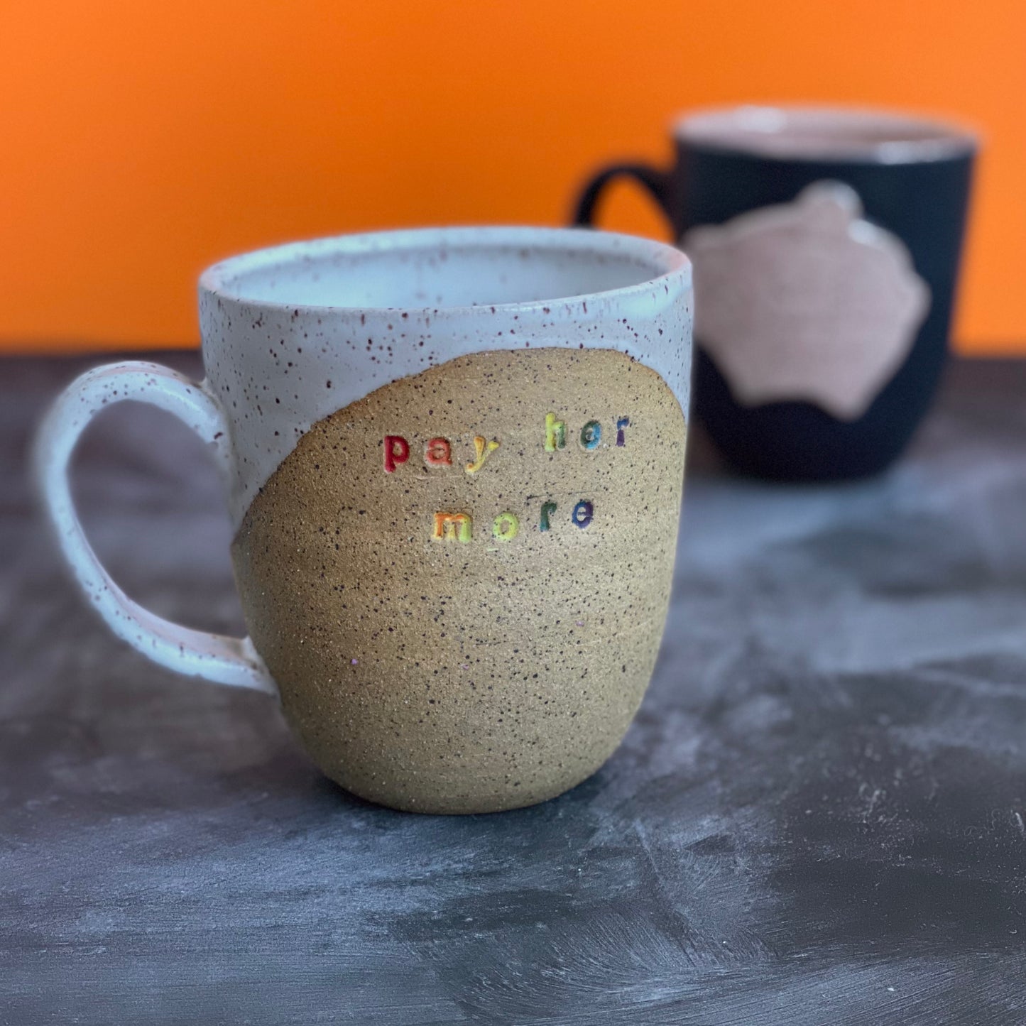 pay her more mug with white glaze and rainbow text