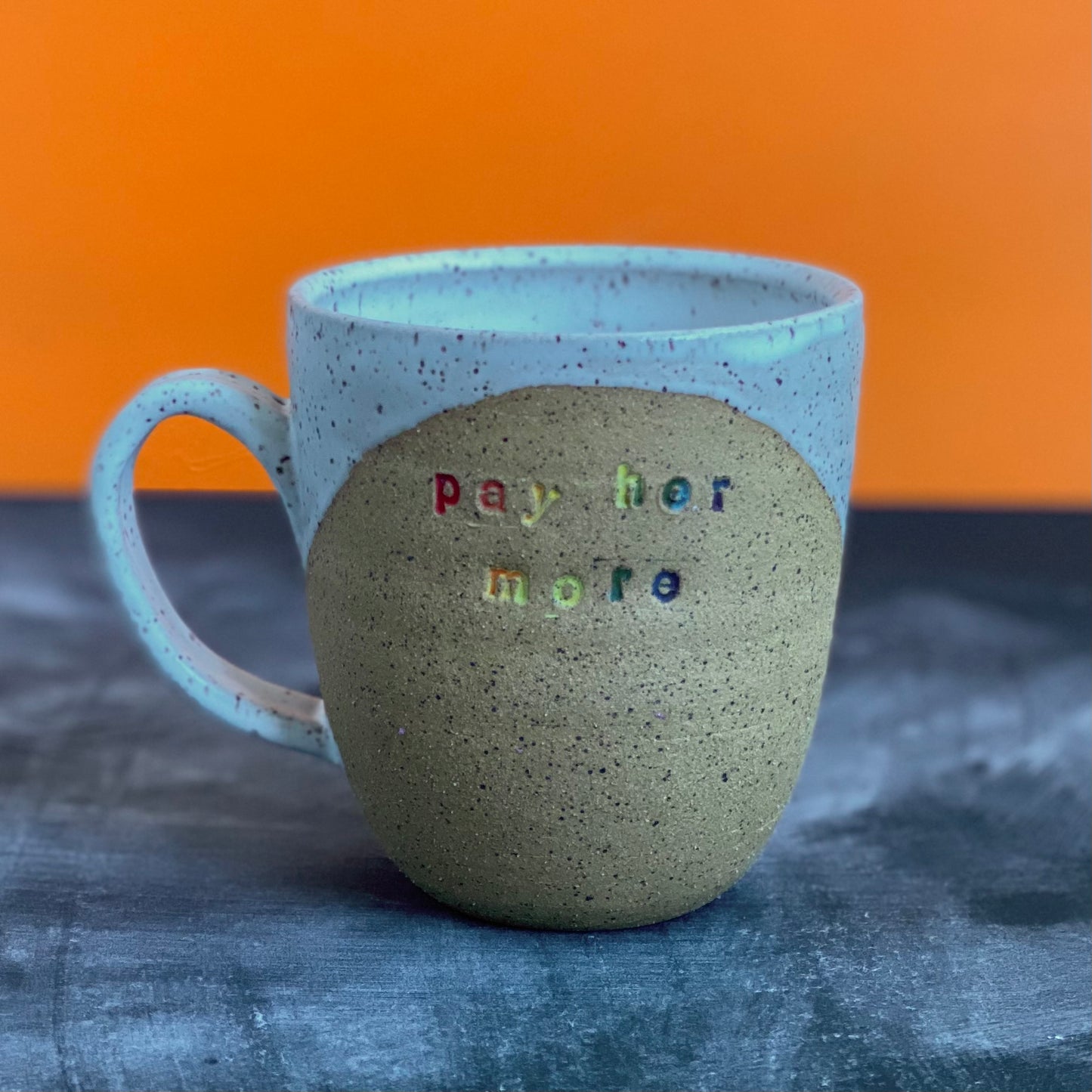 pay her more mug with white glaze and rainbow text