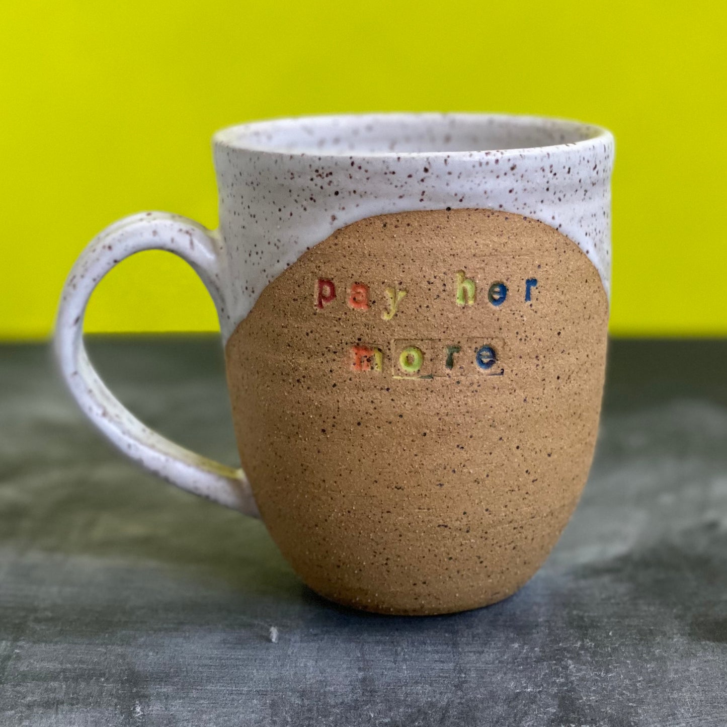pay her more mug with white glaze and rainbow text