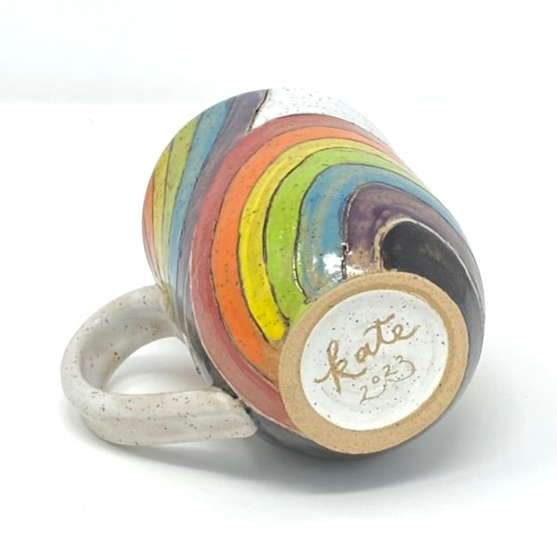 a mug with white glazed interior and handle, and rainbows painted and carved on the outside, as seen from the bottom, carved with the artist's name and year.