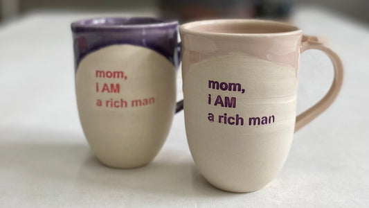 purple glazed mug with pink text, and pink glazed mug with purple text, that both read "mom, i AM a rich man"