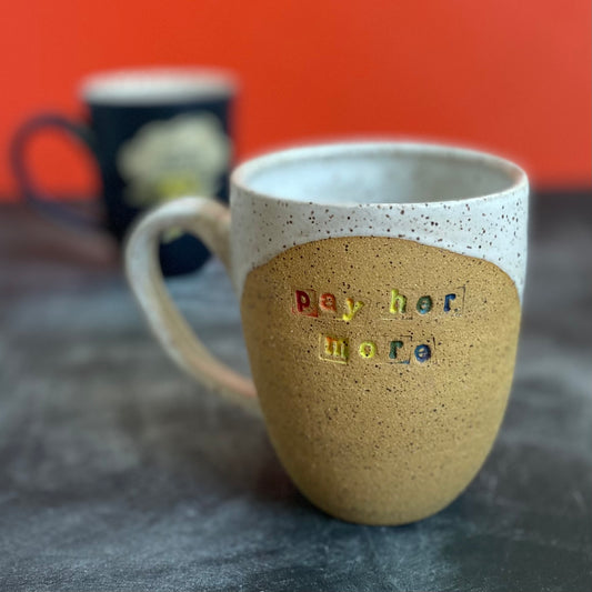 pay her more mug with white glaze and rainbow text