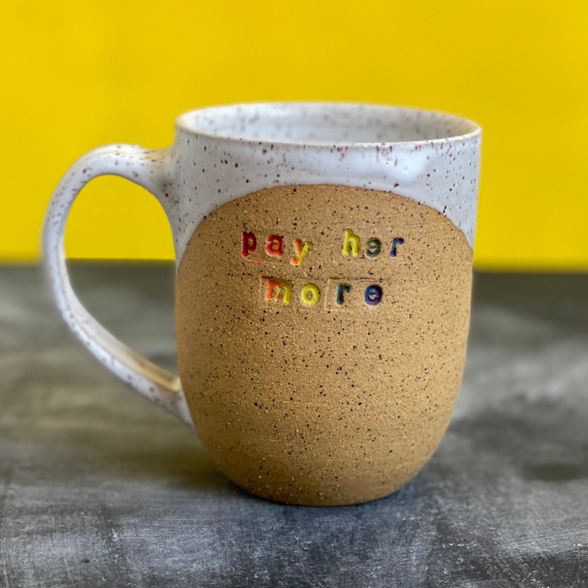 pay her more mug with white glaze and rainbow text