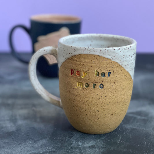 pay her more mug with white glaze and rainbow text