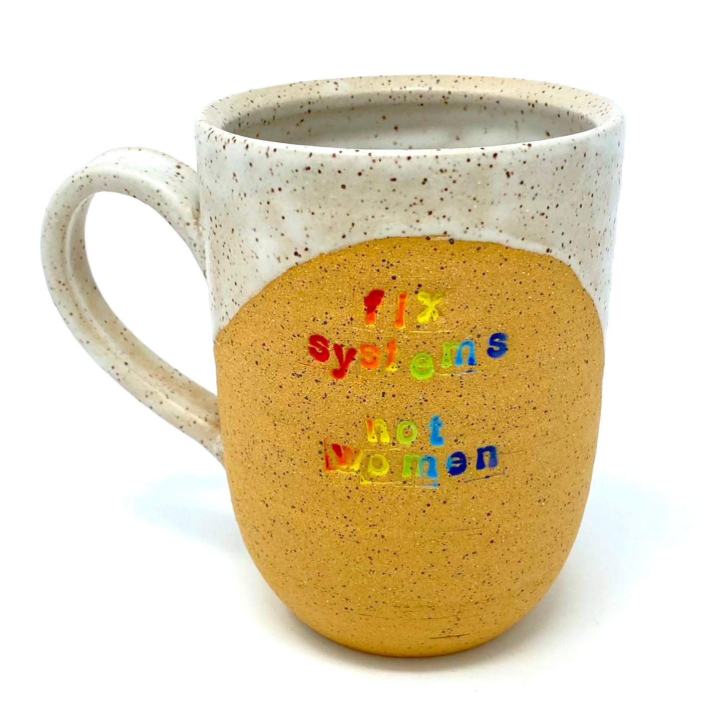 tan stoneware mug as seen from the front. the words "fix systems not women" are inlaid in rainbow color, with white glaze swooping from the inside around the rim and down the handle.